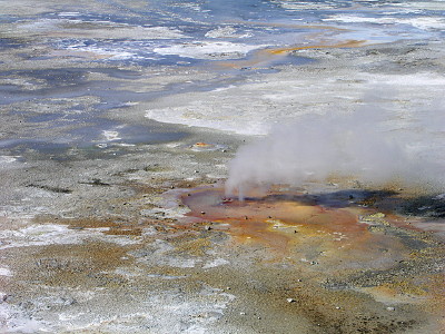 [A close view of two holes with steam coming from them. The ground around the hoels is shades of red-brown while further out the ground appears to be blue and white (from the salt build-ups).]